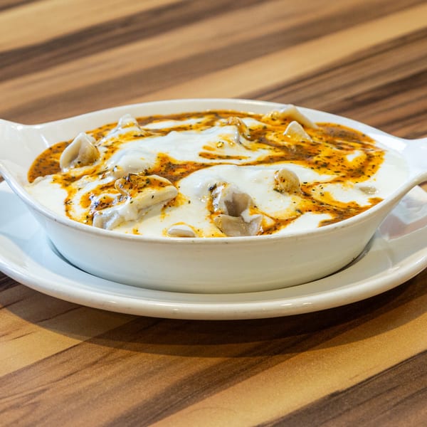 Turkish manti dumplings with yogurt and spiced oil in a white bowl on a wooden table.