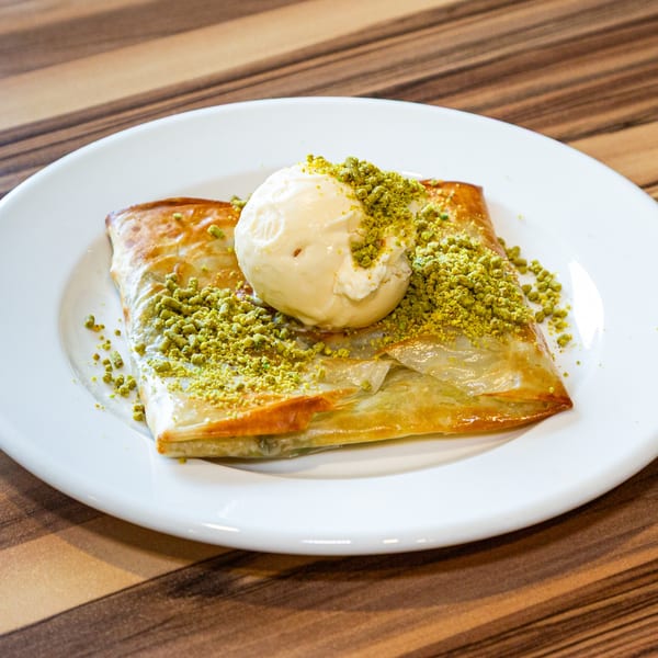 Turkish dessert with a scoop of vanilla ice cream and crushed pistachios on a white plate.