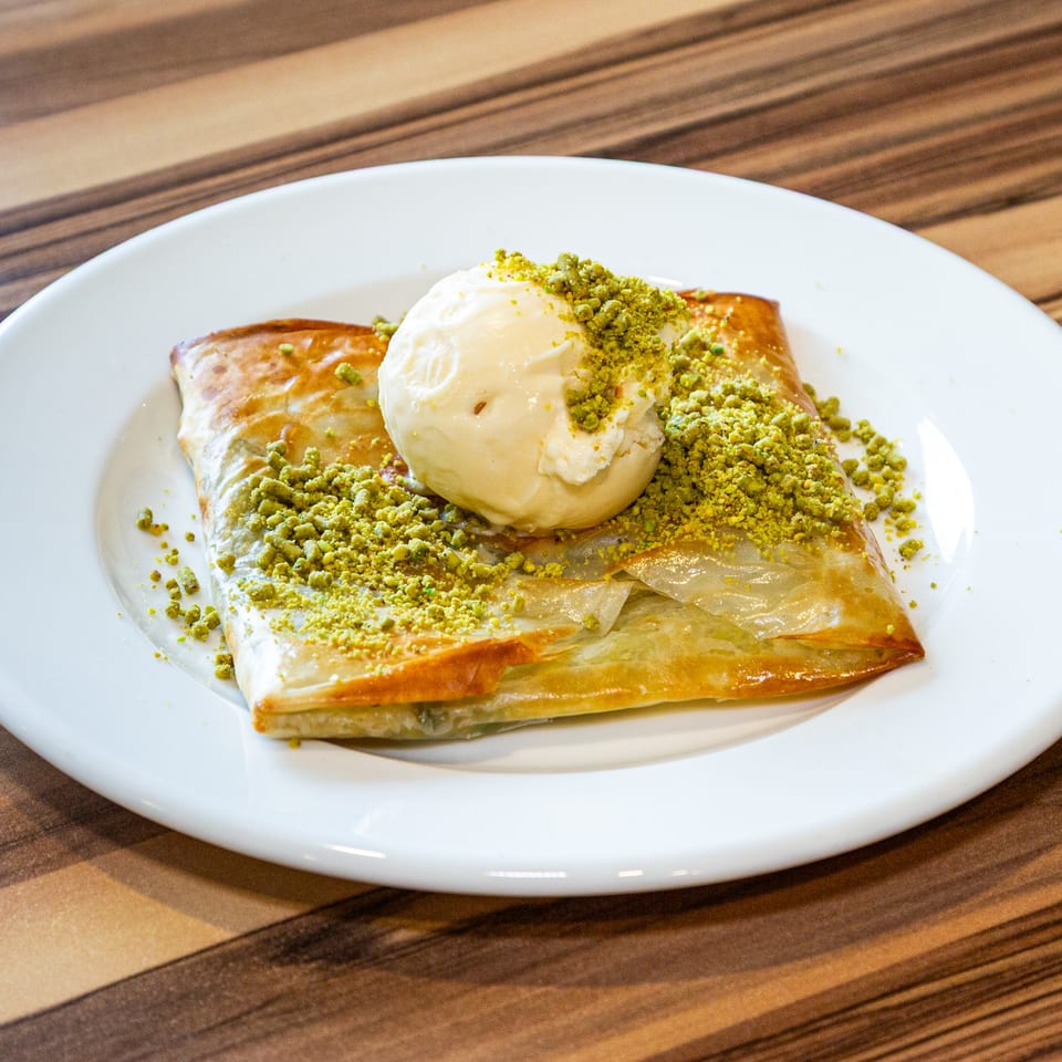 Turkish dessert with a scoop of vanilla ice cream and crushed pistachios on a white plate.