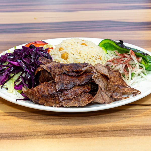 Turkish Doner Kebab with rice, red cabbage salad, grilled pepper, and onions on a white plate.