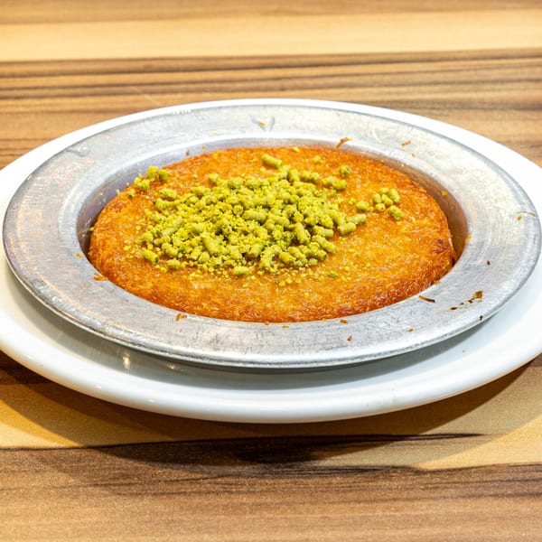 Golden Turkish kunefe dessert with bright green pistachio crumbles in a metal serving dish.