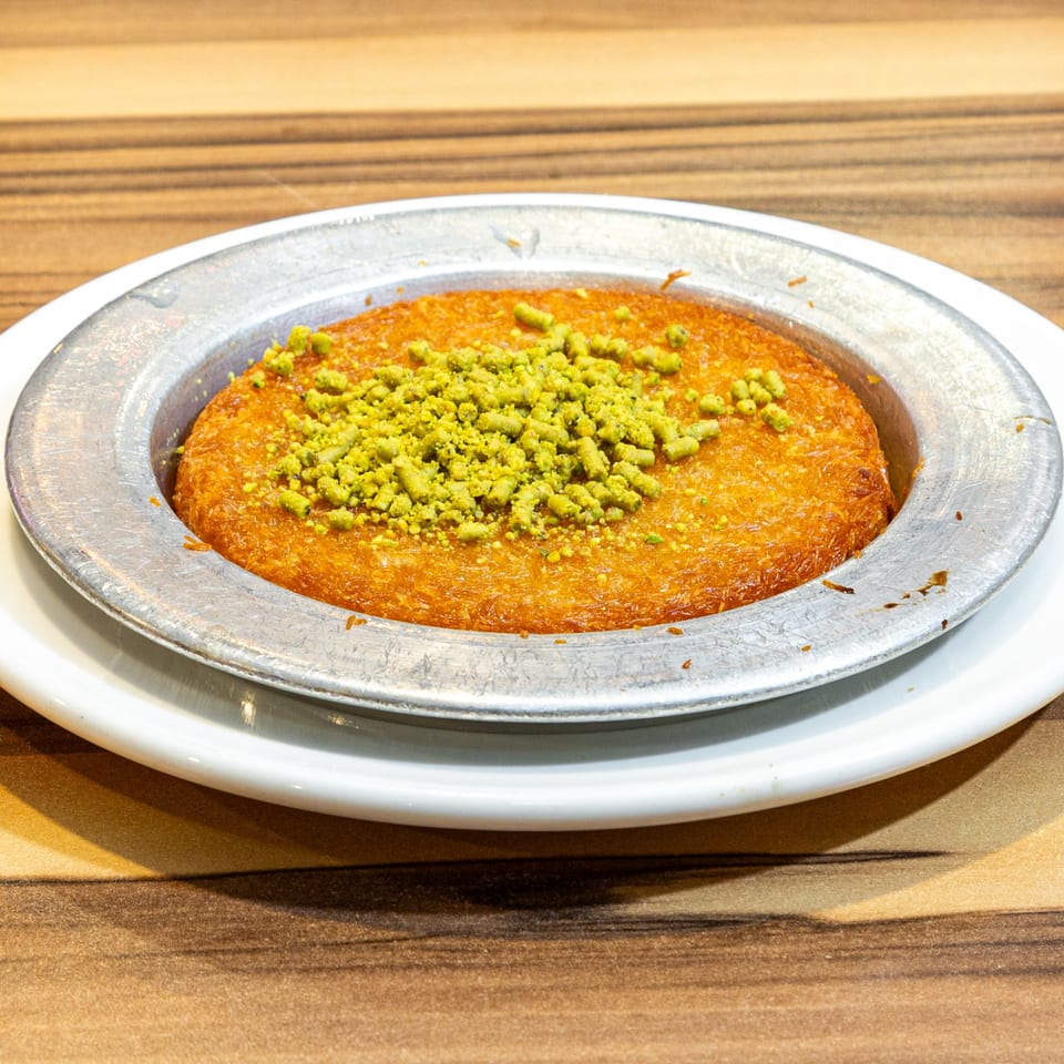 Golden Turkish kunefe dessert with bright green pistachio crumbles in a metal serving dish.