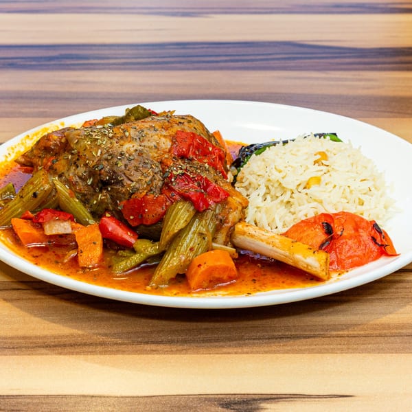 Turkish lamb shank with vegetables and rice, served on a white plate.