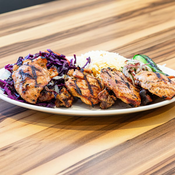 Grilled chicken pieces, rice, red cabbage salad, and a green pepper on a white plate.