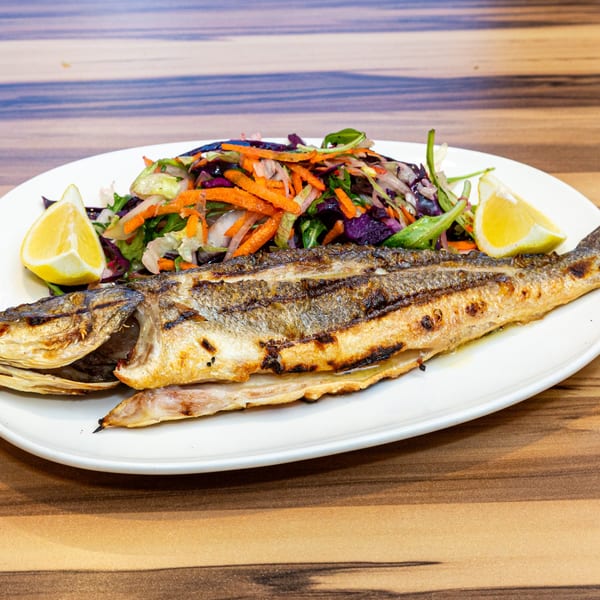 Grilled whole fish with a side of colorful salad and lemon wedges on a white plate.