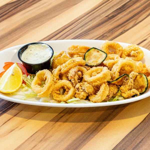 Crispy fried calamari and zucchini on a white plate with tartar sauce, lemon, and lettuce.