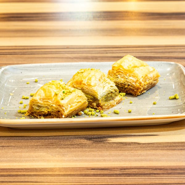 Three pieces of Turkish baklava with pistachio sprinkles on a rectangular plate.