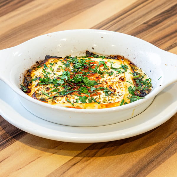 Baked feta cheese with herbs and spices in a white oval dish on a wooden table.