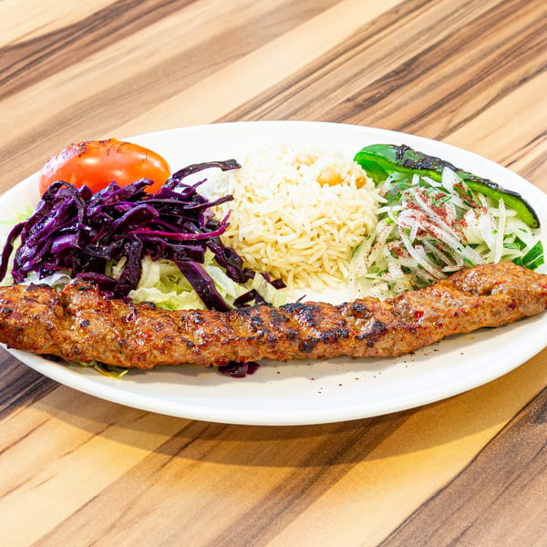 Adana kebab with rice, grilled tomato, green pepper, red cabbage, and onion salad.